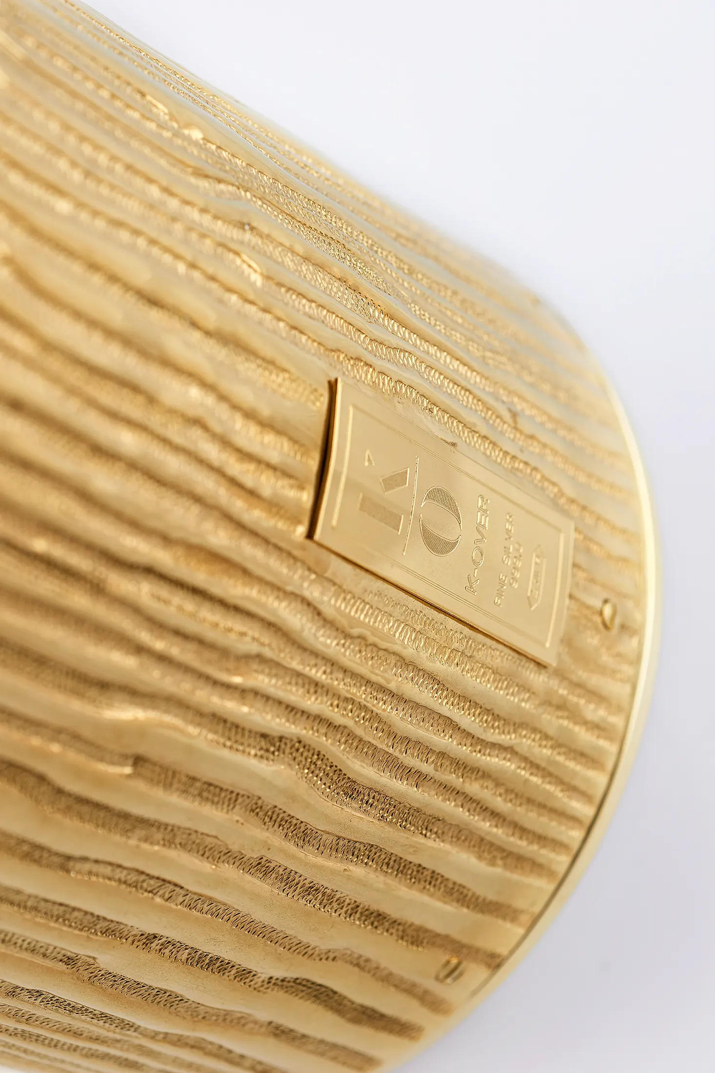 Close-up Studio still life photograph of a gold bottle cover by K-Over on a white background – product photography by Memento Agency