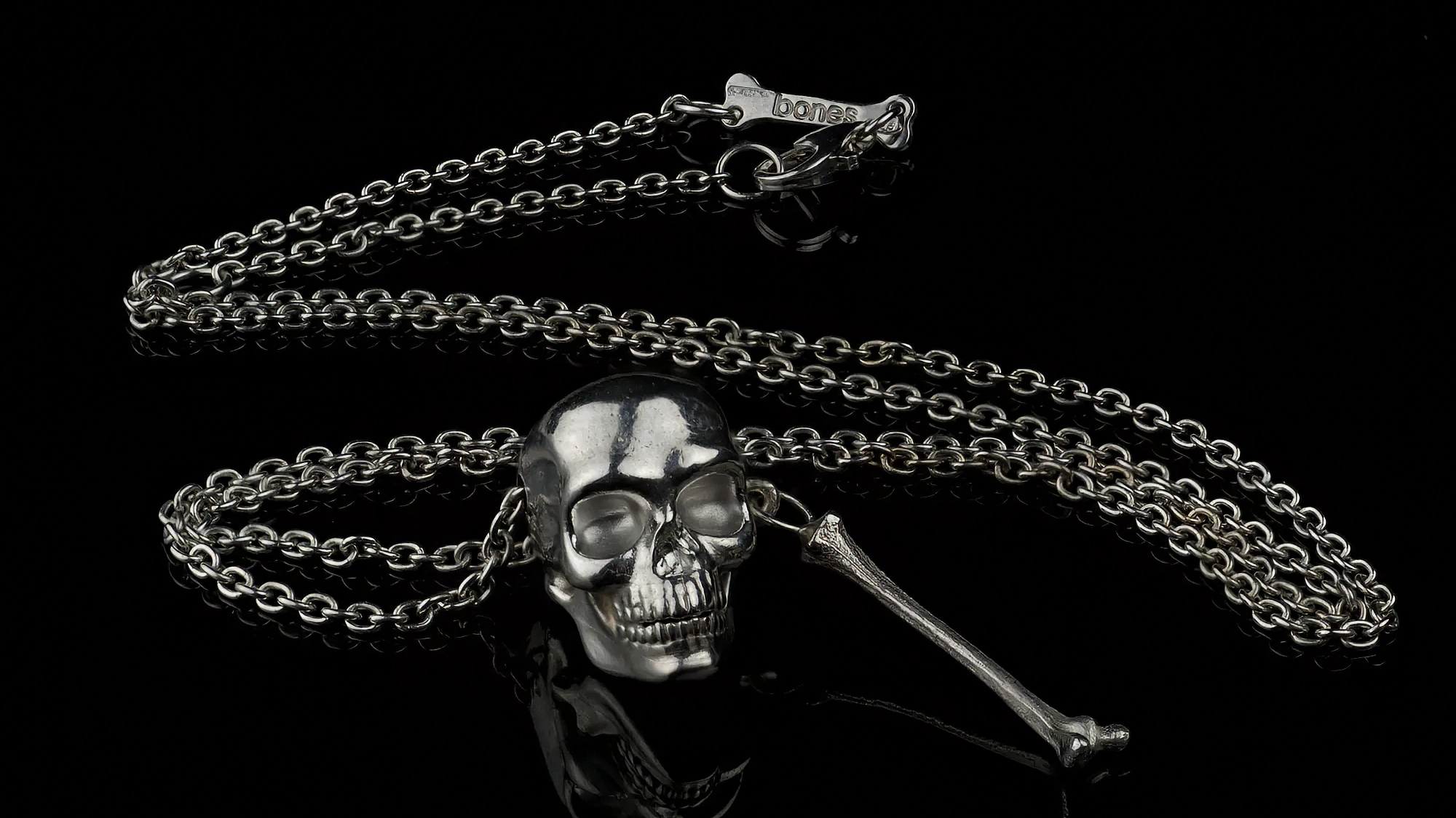 Low key still life photography of a silver oxidized skull and crossbone pendant by Bones Firenze on a black background – dramatic lighting, minimalist composition