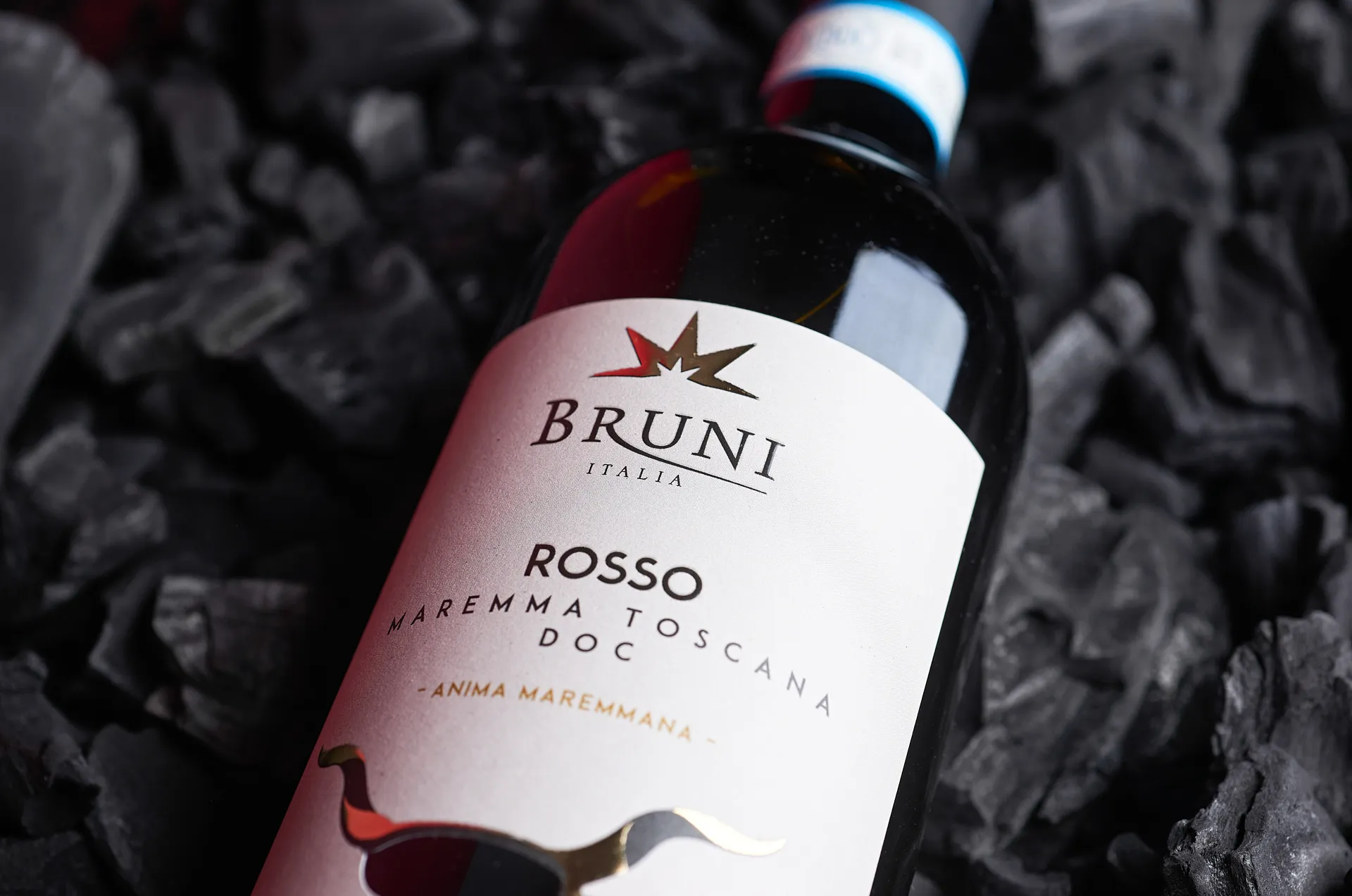 Close-up ambient still life photo of Maremma Toscana DOC wine bottle lying on charcoal – elegant Tuscan wine product photography