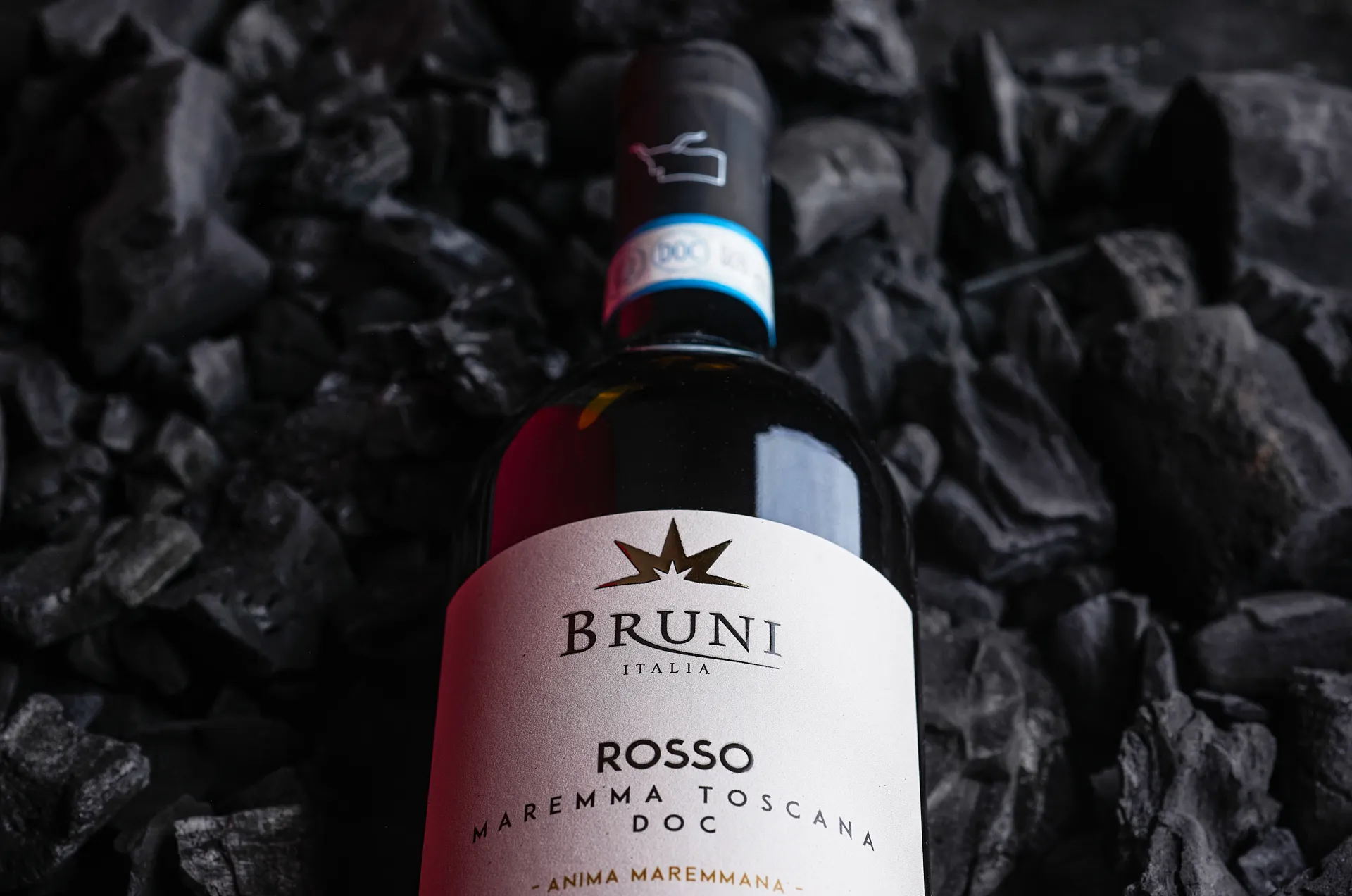Close-up ambient still life photo of Maremma Toscana DOC wine bottle lying on charcoal – elegant Tuscan wine product photography