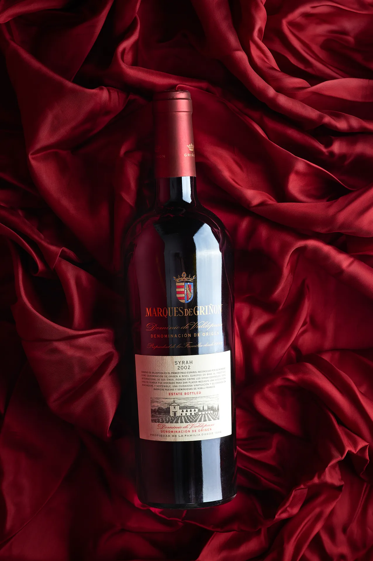 Ambient still life photo of Syrah wine bottle from Marques de Grinon lying on red velvet – elegant Spanish wine product photography